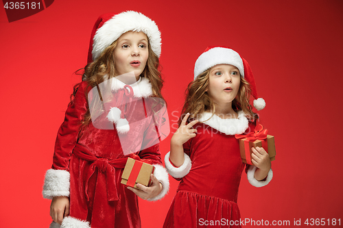 Image of Two happy girls in santa claus hats with gift boxes