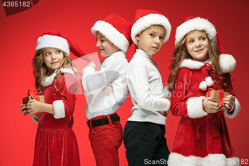 Image of Two happy girls and boys in santa claus hats with gift boxes