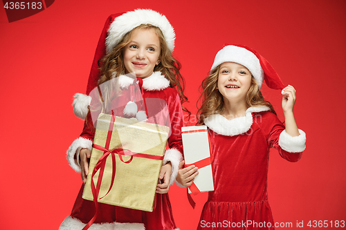 Image of Two happy girls in santa claus hats with gift boxes