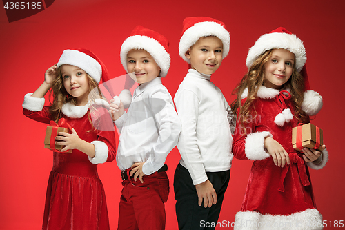 Image of Two happy girls and boys in santa claus hats with gift boxes