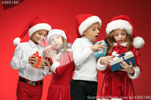Image of Two happy girls and boys in santa claus hats with gift boxes