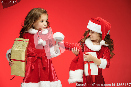 Image of Two happy girls in santa claus hats with gift boxes at studio