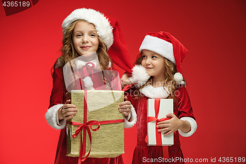 Image of Two happy girls in santa claus hats with gift boxes at studio