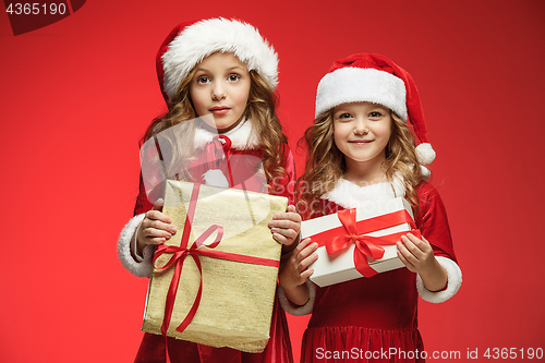 Image of Two happy girls in santa claus hats with gift boxes at studio