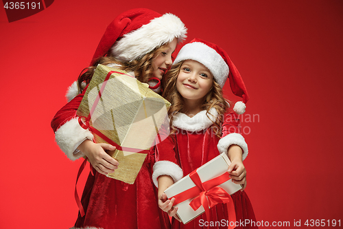 Image of Two happy girls in santa claus hats with gift boxes at studio