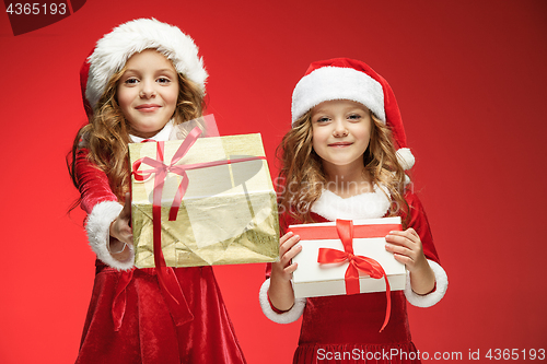 Image of Two happy girls in santa claus hats with gift boxes at studio