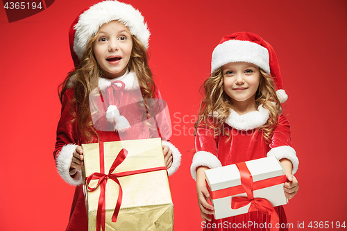 Image of Two happy girls in santa claus hats with gift boxes at studio