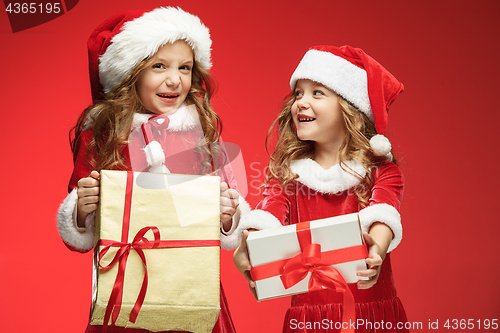 Image of Two happy girls in santa claus hats with gift boxes at studio