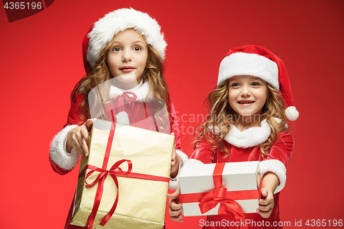 Image of Two happy girls in santa claus hats with gift boxes at studio