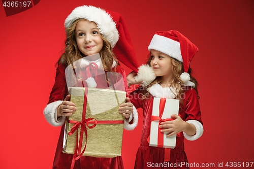 Image of Two happy girls in santa claus hats with gift boxes at studio