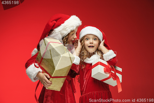 Image of Two happy girls in santa claus hats with gift boxes at studio