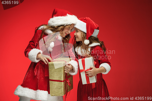 Image of Two happy girls in santa claus hats with gift boxes at studio