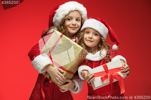 Image of Two happy girls in santa claus hats with gift boxes at studio