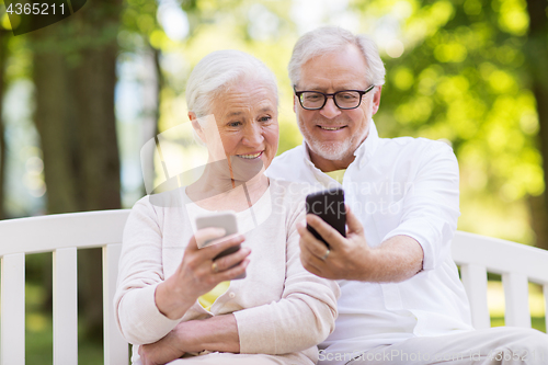 Image of happy senior couple with smartphones at park