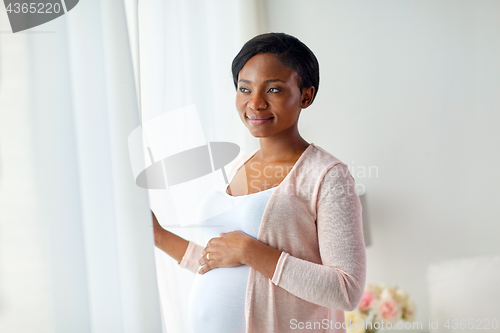 Image of pregnant woman looking through window at home