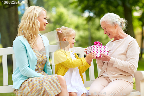Image of happy family giving present to grandmother at park
