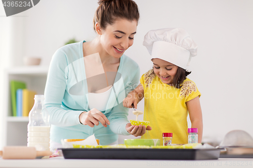 Image of happy mother and daughter baking cupcakes at home