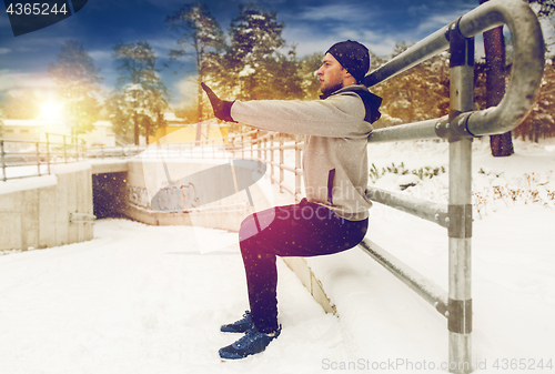 Image of sports man doing squats at fence in winter