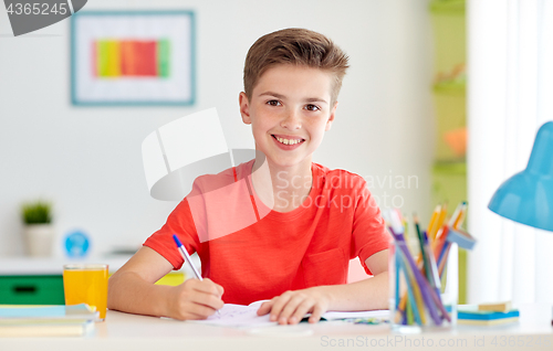 Image of happy student boy writing to notebook at home