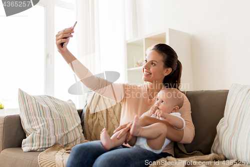 Image of happy mother with baby boy taking selfie at home