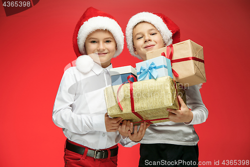 Image of Two happy boys in santa claus hats with gift boxes at studio