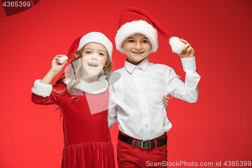 Image of Two happy boy and girl in santa claus hats with gift boxes at studio