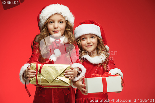 Image of Two happy girls in santa claus hats with gift boxes at studio