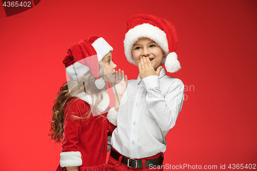 Image of Two happy boy and girl in santa claus hats with gift boxes at studio