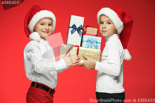 Image of Two happy boys in santa claus hats with gift boxes at studio