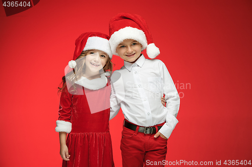 Image of Two happy boy and girl in santa claus hats with gift boxes at studio