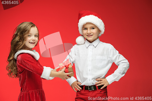 Image of Two happy boy and girl in santa claus hats with gift boxes at studio