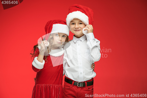 Image of Two happy boy and girl in santa claus hats with gift boxes at studio