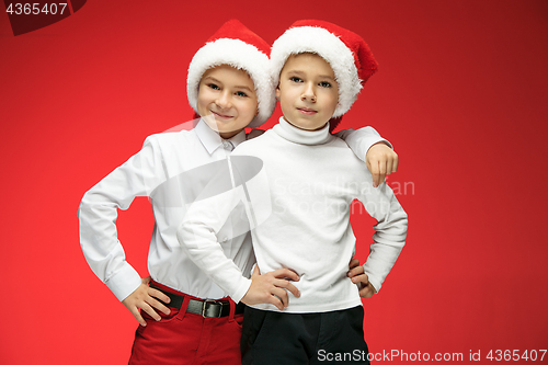 Image of Two happy boys in santa claus hats with gift boxes at studio