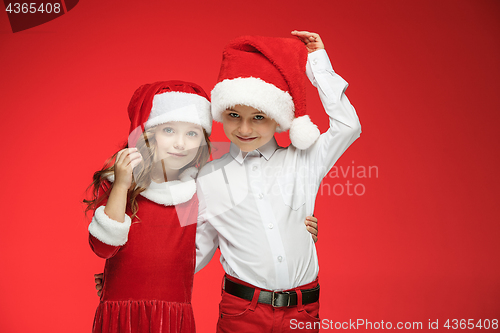 Image of Two happy boy and girl in santa claus hats with gift boxes at studio