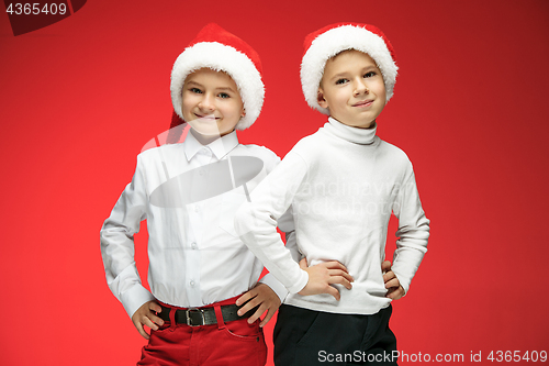 Image of Two happy boys in santa claus hats with gift boxes at studio