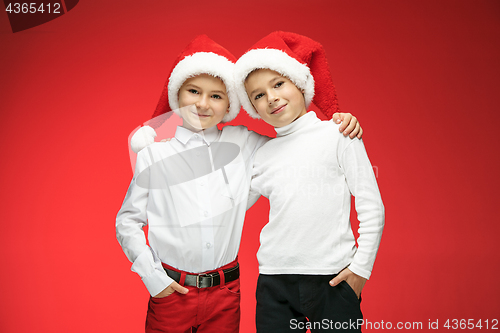 Image of Two happy boys in santa claus hats with gift boxes at studio