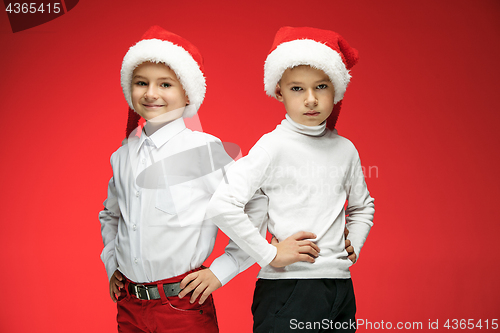 Image of Two happy boys in santa claus hats with gift boxes at studio