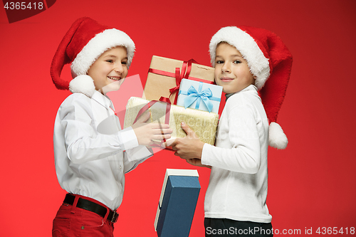 Image of Two happy boys in santa claus hats with gift boxes at studio