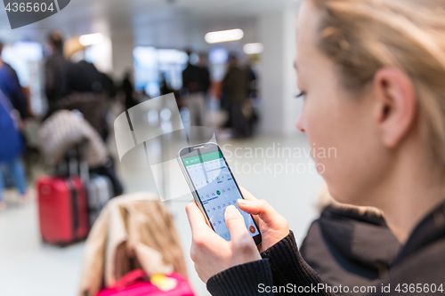 Image of Woman checking information on mobile phone sitting in airport terminal.