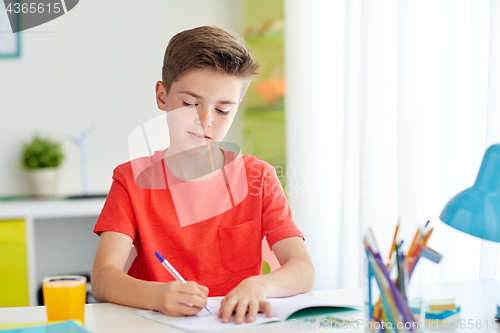 Image of happy student boy writing to notebook at home