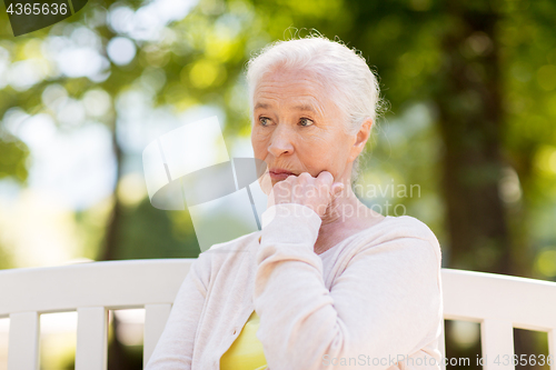 Image of sad senior woman sitting on bench at summer park