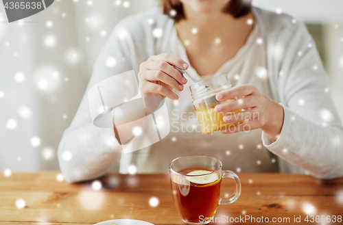 Image of close up of woman adding honey to tea with lemon