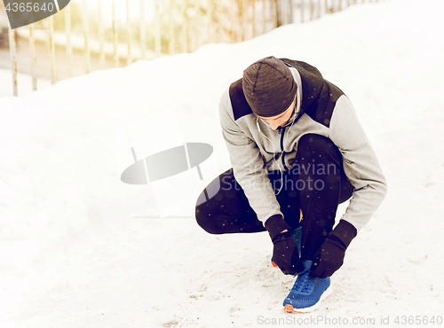 Image of man with earphones tying sports shoe in winter