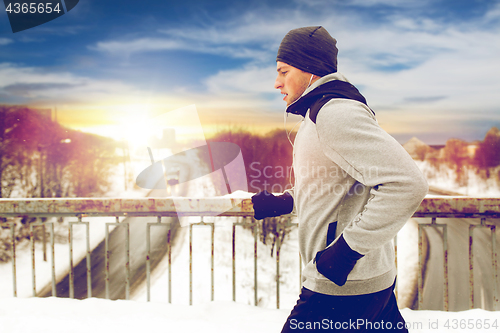 Image of man in earphones running along winter bridge