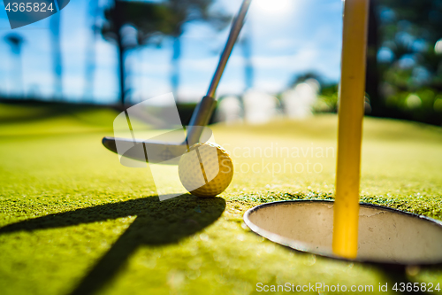 Image of Mini Golf yellow ball with a bat near the hole at sunset