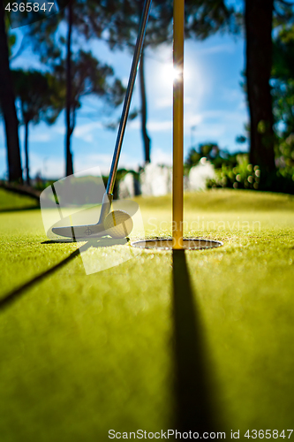 Image of Mini Golf yellow ball with a bat near the hole at sunset