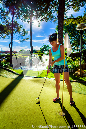 Image of Mini Golf - Woman playing Golf on green grass at sunset