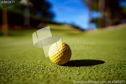 Image of Mini Golf yellow ball on green grass at sunset