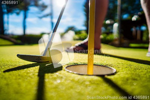 Image of Mini Golf yellow ball with a bat near the hole at sunset