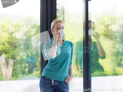 Image of young woman drinking morning coffee by the window